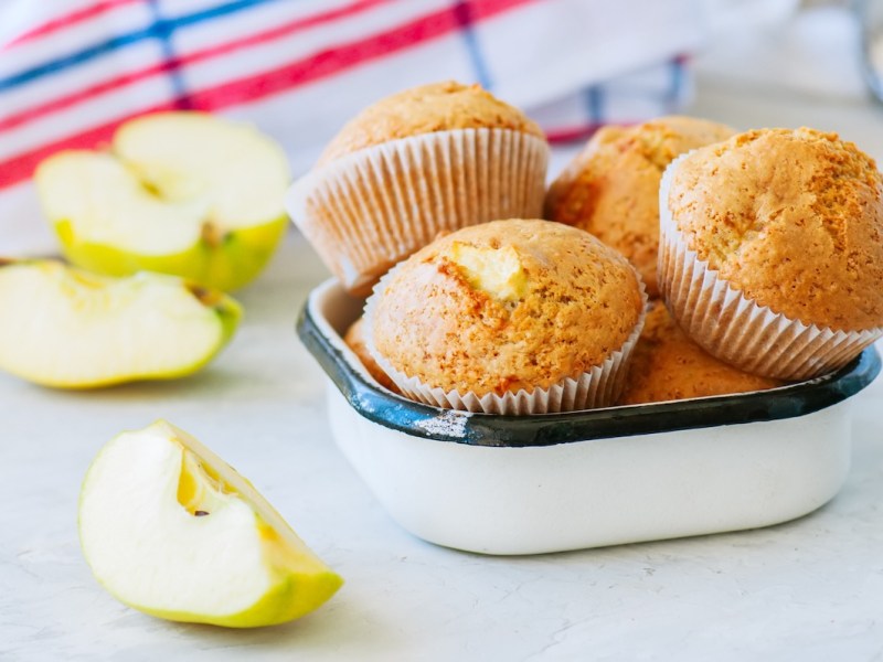 a few apple oatmeal muffins in a lunchbox, next to them small cut apples