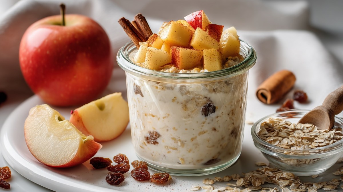 Cinnamon apple overnight oats in a glass topped with apple pieces. Some ingredients around it.