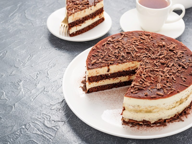An eggnog tiramisu cake with a slice taken out. Next to it is a cup of coffee.