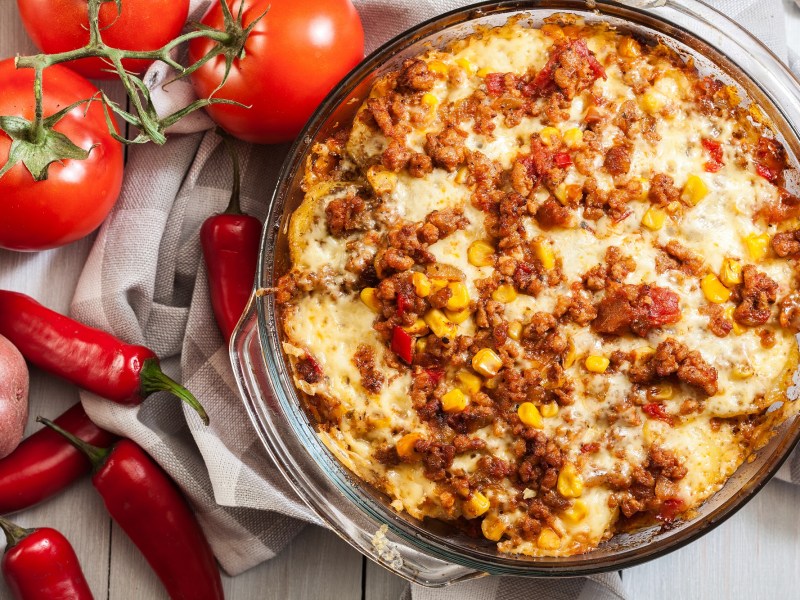 Mexican-style ground beef and potato casserole in a baking dish, next to tomatoes, chilies and potatoes.