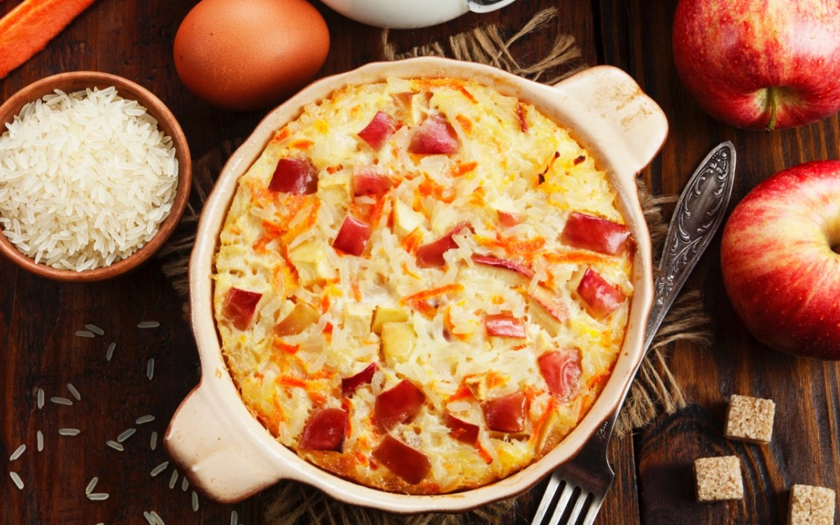 An overhead view of a rice pudding bake with apples. Around it are ingredients.