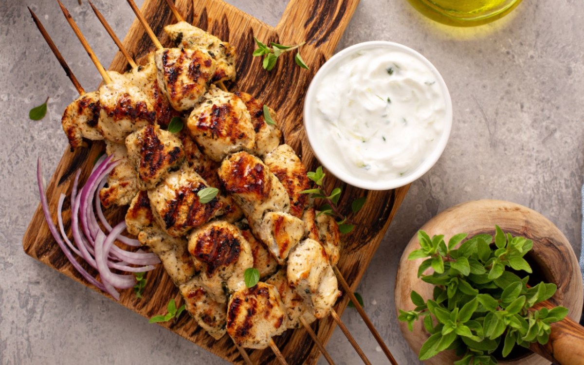 Several souvlaki. Next to them are onions and a bowl of tzatziki.
