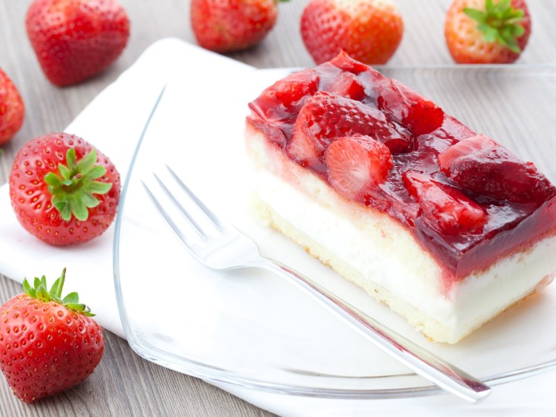 A piece of sheet pan strawberry cream cake on a plate, next to it a fork and fresh strawberries.
