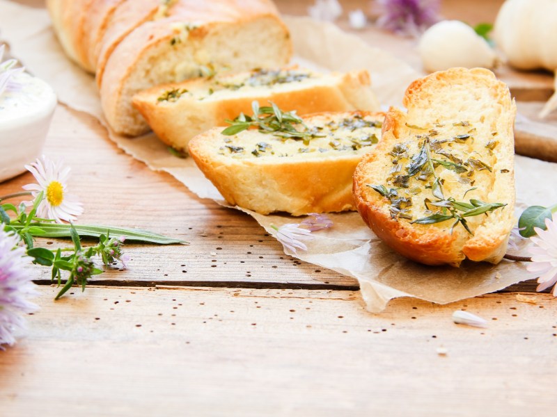 A sliced homemade herb baguette, next to fresh wildflowers