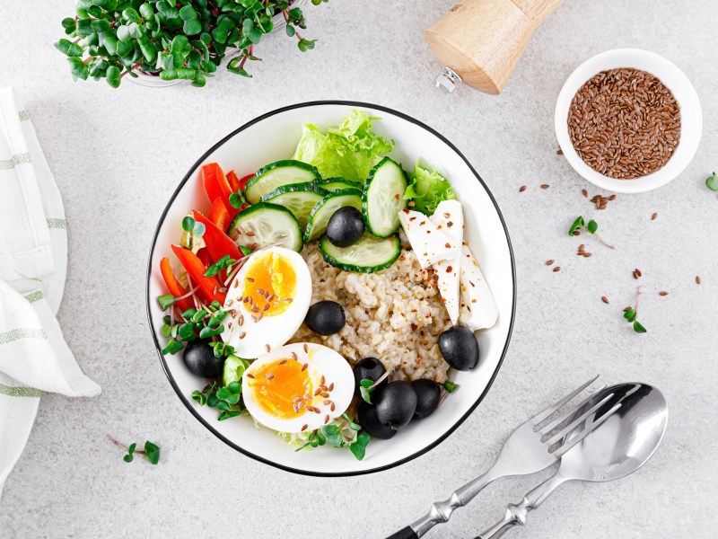 An oatmeal bowl with feta and egg, with bell peppers, lettuce, cucumbers, and olives.
