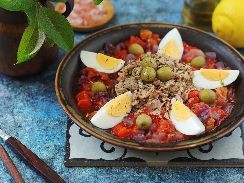Tunisian grilled salad Slata Mechouia, served with tuna and eggs, on a dark plate.
