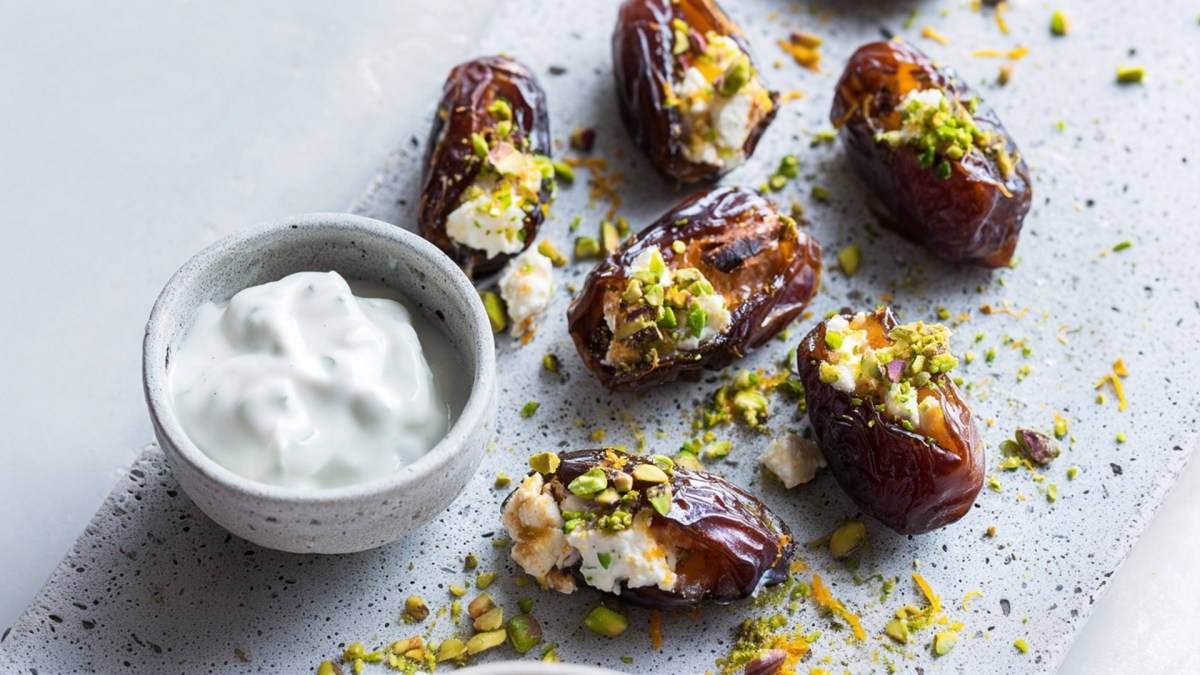 A gray stone plate with some stuffed dates on it, which were previously grilled date and feta skewers. The dates are served with a small bowl of yogurt dip.