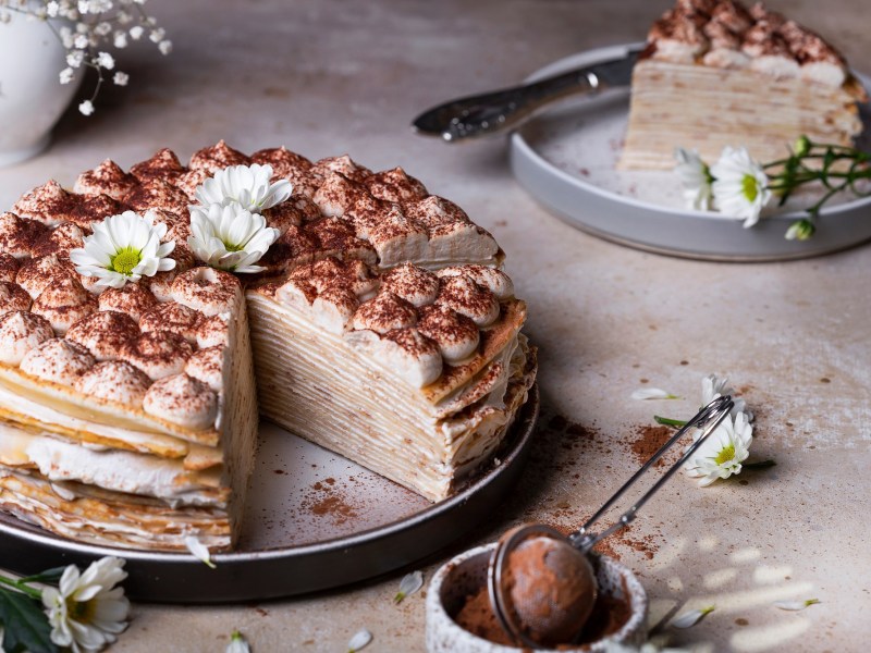 Tiramisu pancake cake, with a piece removed, on a cake plate.